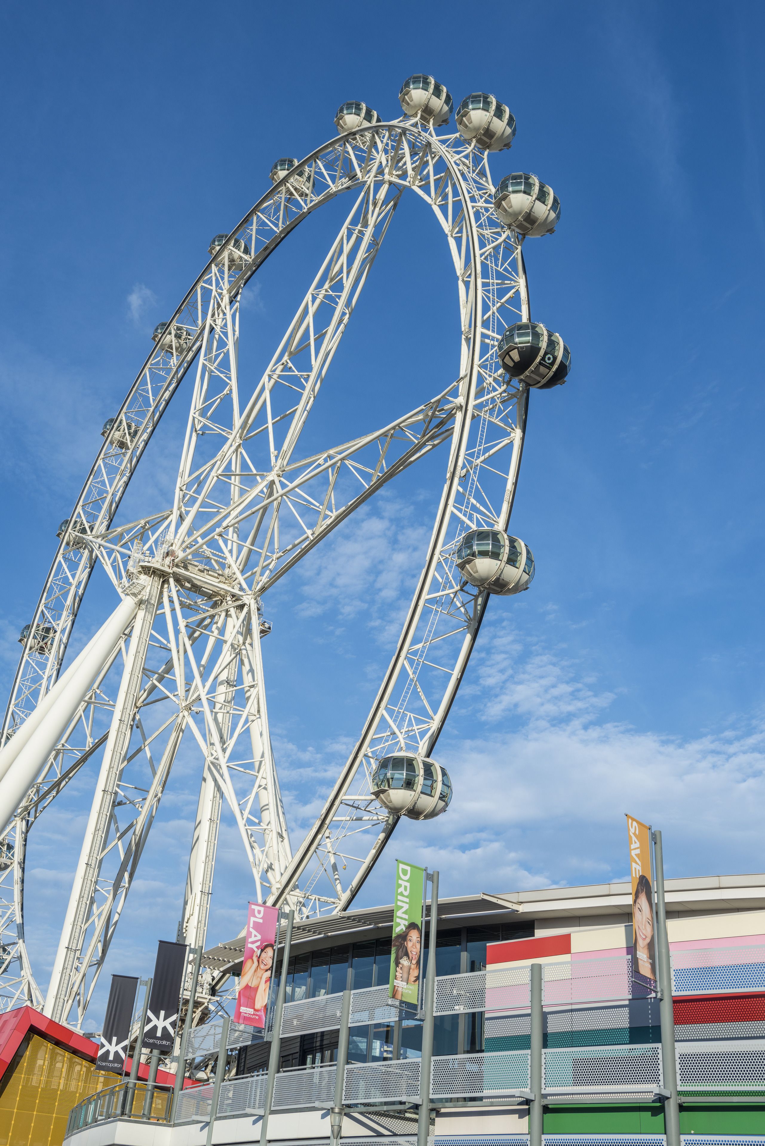 A Ferris wheel with cabins, a clear sky, and a building with colorful signage.