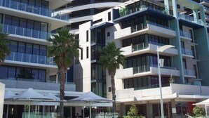 A modern hotel with a curved facade, multiple balconies, and a central courtyard with palm trees. - AKOM AT Docklands (Docklands)