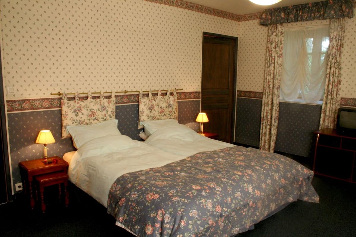 A bedroom with a bed, two bedside lamps, a television, and floral-patterned curtains.