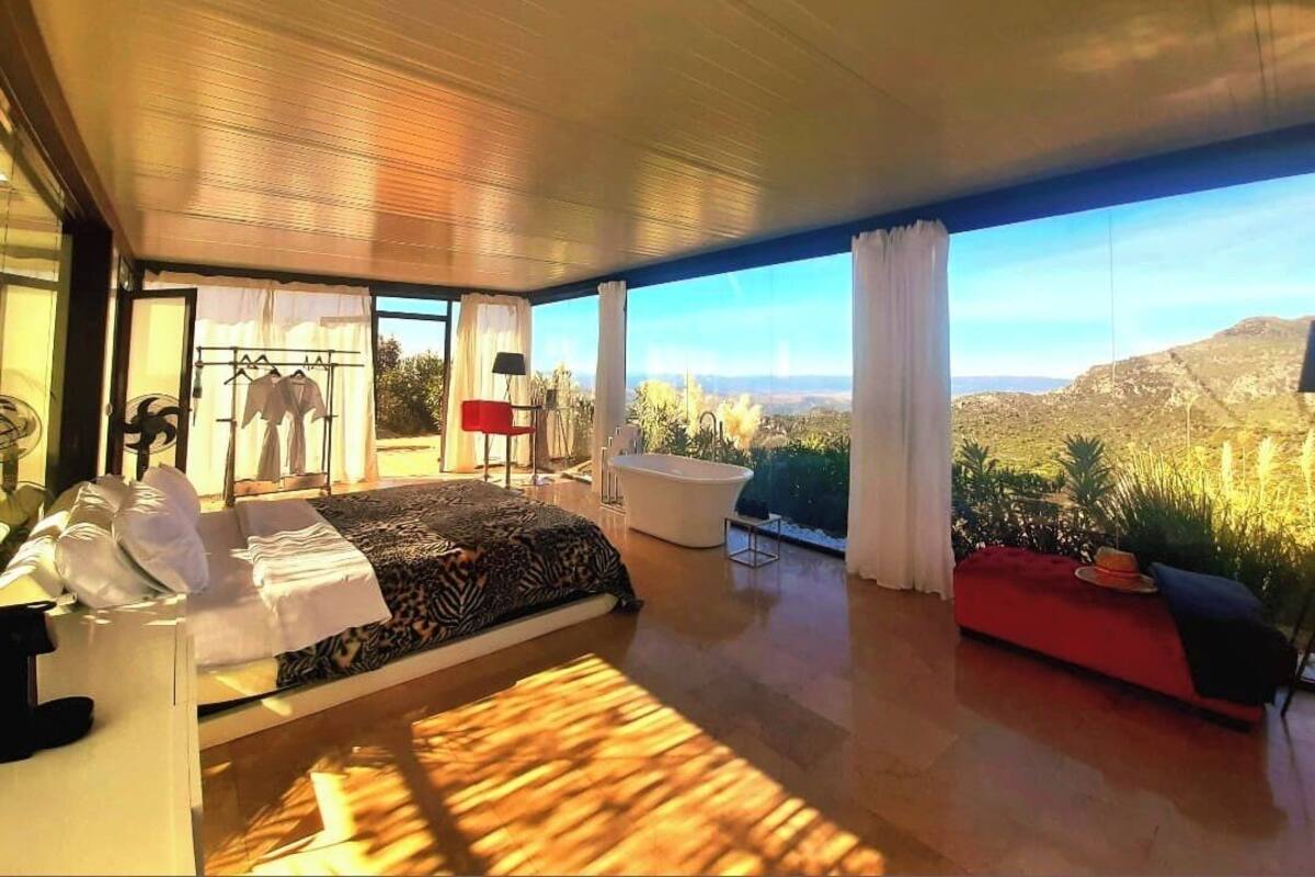 A spacious bedroom with a large bed, a red sofa, a bathtub, and a view of the mountains.