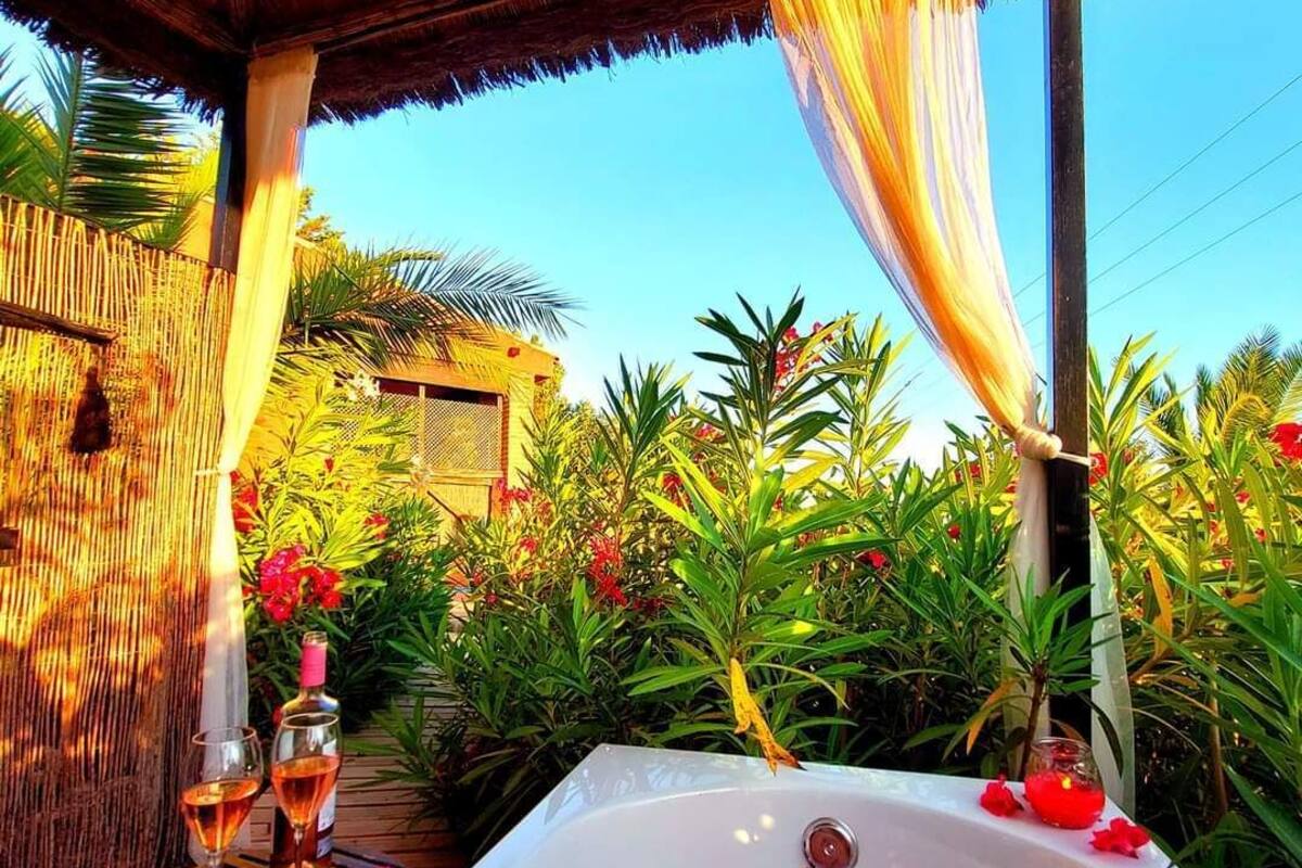 A hot tub with rose petals floating on the water, surrounded by lush greenery and a bamboo fence.