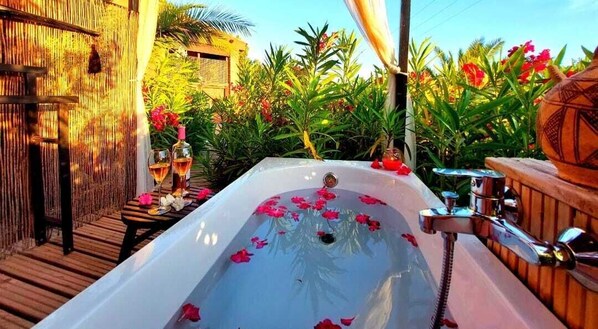 A spa area with a bathtub filled with rose petals, surrounded by lush greenery and a wooden deck. - DDG Retreat (Casares)