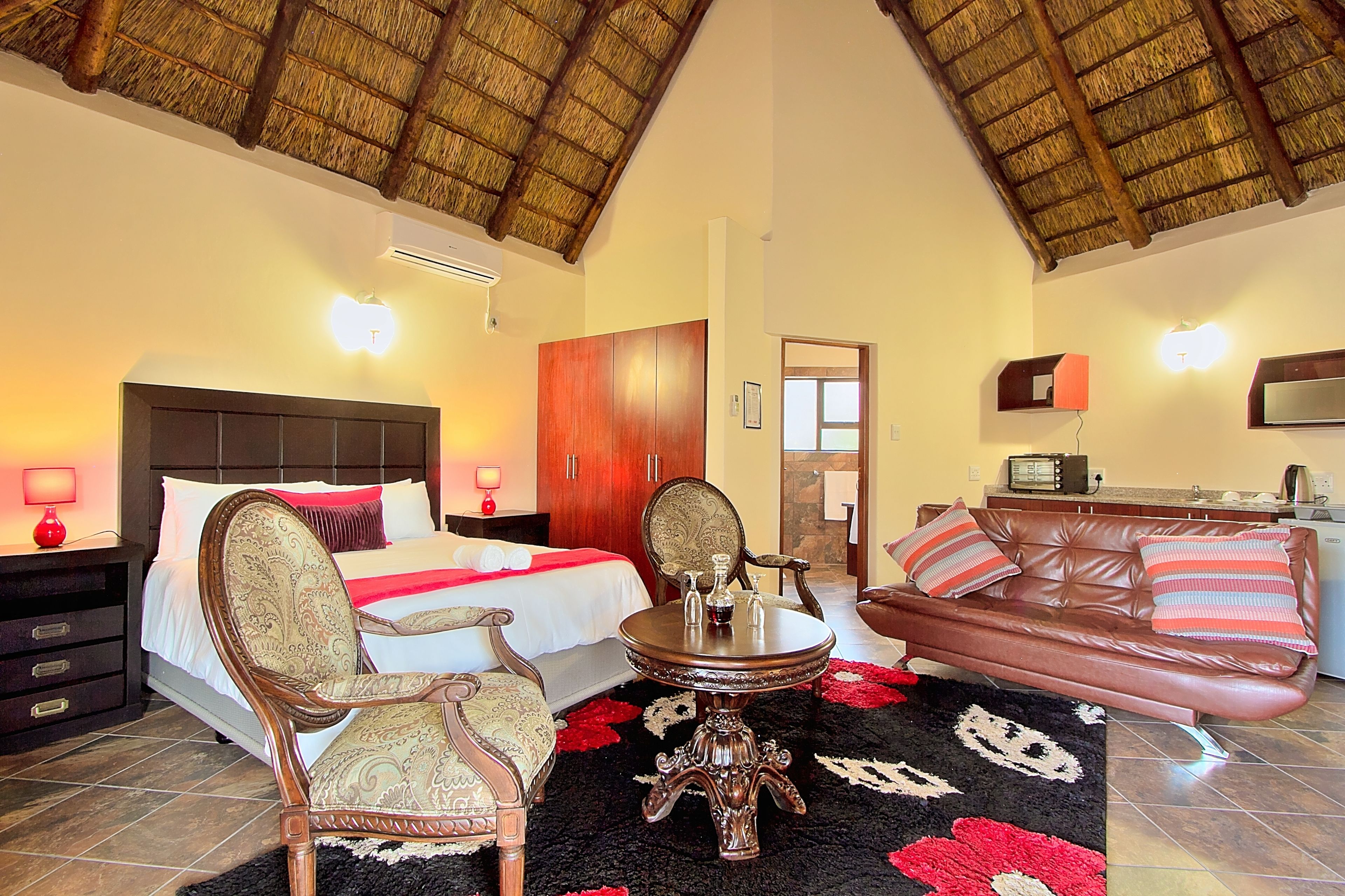 A hotel room with a bed, a sitting area with a sofa and armchairs, a dining table, and a kitchen area.