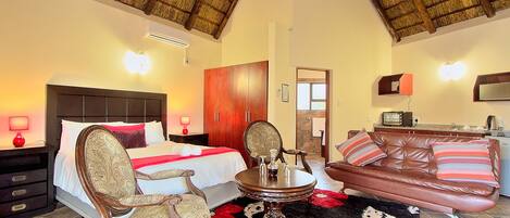 A hotel room with a bed, a sitting area with a sofa and armchairs, a dining table, and a kitchen area.
