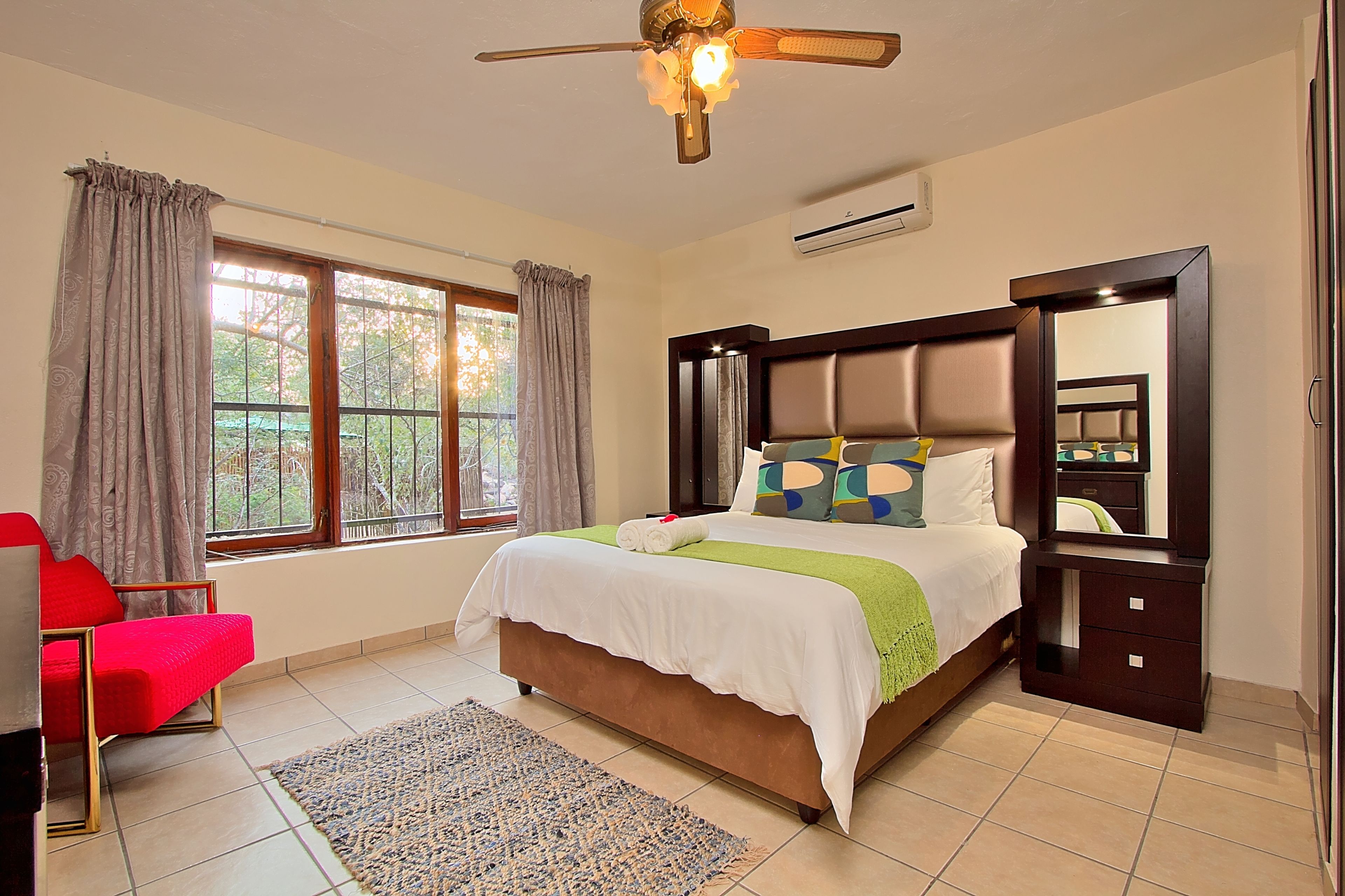 A bedroom with a bed, a nightstand, a chair, a window with curtains, and a ceiling fan.