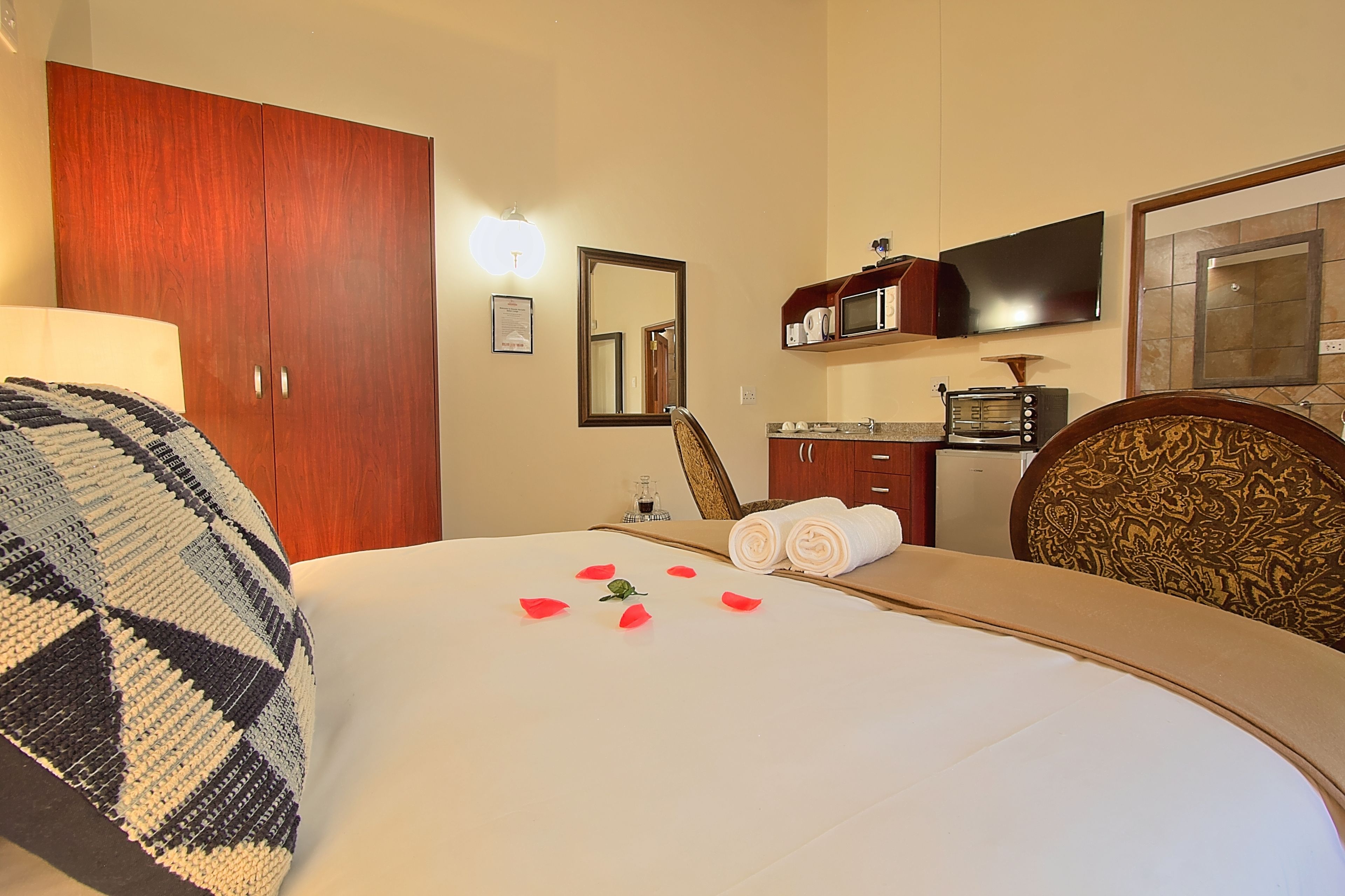 A hotel room with a bed, a wooden wardrobe, a television, a microwave, and a bathroom.