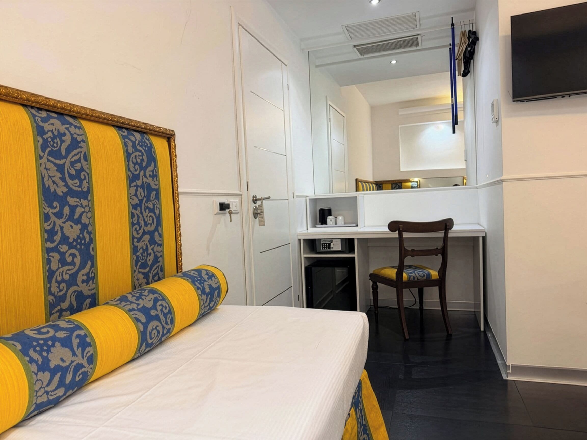Et hotelværelse med seng, skrivebord, stol og fjernsyn.