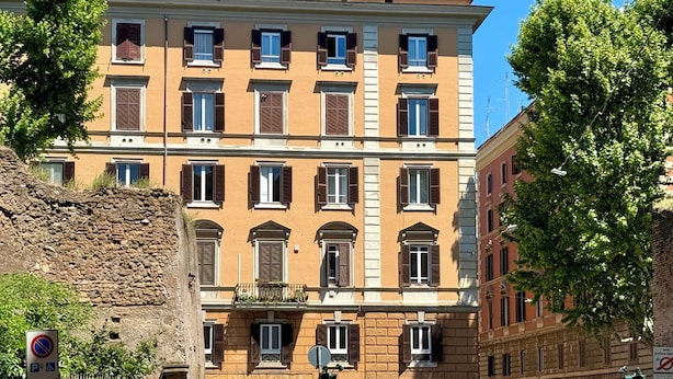 Ein mehrstöckiges Gebäude mit einheitlichem Baustil, das eine Reihe von Fenstern mit Fensterläden, einen Balkon und eine Straßenlaterne zeigt.