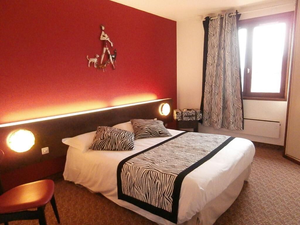 A hotel room with a bed, a chair, a headboard with lights, a zebra-patterned bedspread, a wall decoration of a person walking a dog, and a window with curtains.