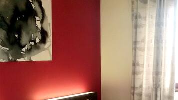 A hotel room with two beds, a red accent wall, and a painting.