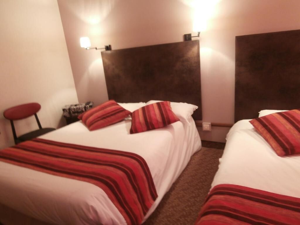 A hotel room with two beds, each with a red-striped bedspread, a dark headboard, and a nightstand with a lamp.