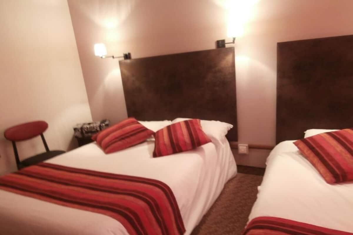 A hotel room with two beds, each with a red-striped bedspread, a dark headboard, and a nightstand with a lamp.