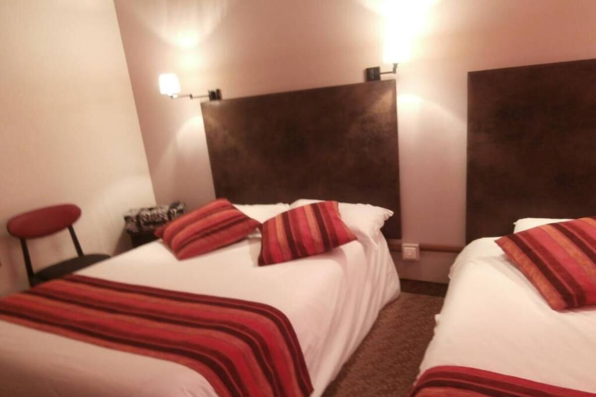 Habitación de hotel con dos camas, cada una con cubrecama a rayas rojas, cabecero oscuro y mesita de noche con lámpara.