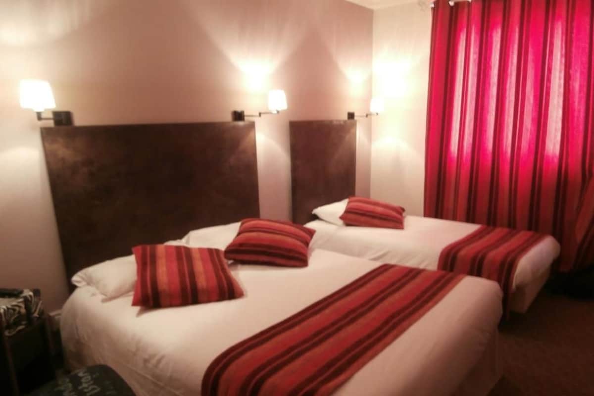 A hotel room with two beds, each with a red-striped blanket, a headboard, and wall-mounted lights.