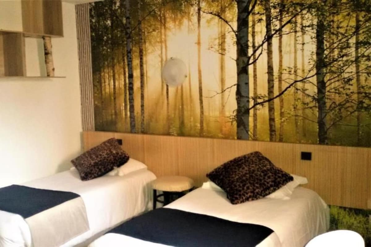 A room with two beds, a small table, and a wall mural of a forest.