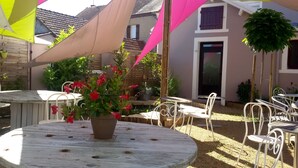 A patio area with round tables and white chairs, surrounded by potted plants and a small fountain. - Hotel Le Merle Blanc (Digoin)