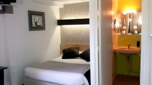 A small, neatly arranged bedroom with a single bed, a framed picture on the wall, and a bathroom visible through an open door. - Hotel Le Merle Blanc (Digoin)