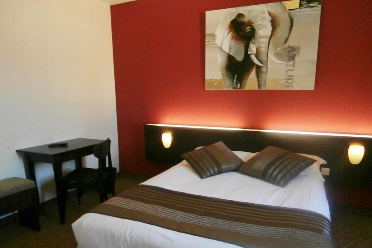 A hotel room with a bed, bedside tables, a desk, and a wall-mounted artwork.
