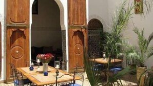 An open courtyard with a wooden table and chairs, surrounded by potted plants and a large wooden door. - Riad Attarine (Fes)