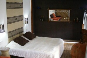 A bed with white and brown bedding, a mirror on the wall, and a small table with a lamp. - Riad Attarine (Fes)