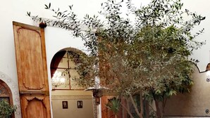 A traditional Moroccan courtyard with a tiled floor, a round table with a blue mosaic border, a pool, and a wooden door. - Riad Attarine (Fes)
