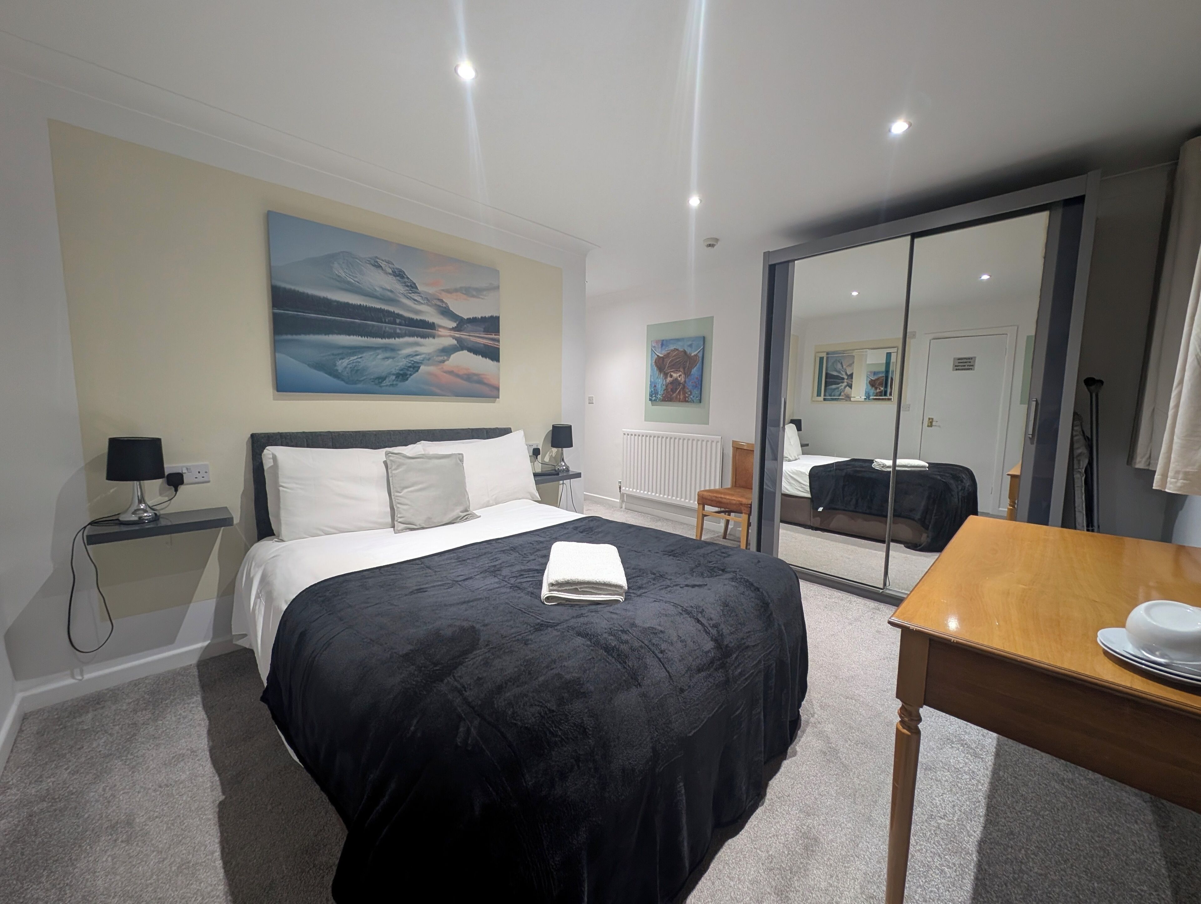 A hotel room with a bed, bedside table, lamp, artwork on the wall, and a sliding door.