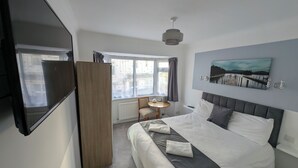 A modern hotel room with a large bed, a desk with a chair, a window with curtains, and a painting on the wall. - Cecil Court Hotel (Bournemouth)