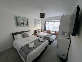 Een hotelkamer met twee bedden, een tafeltje met stoelen, een televisie en kunst aan de muren.