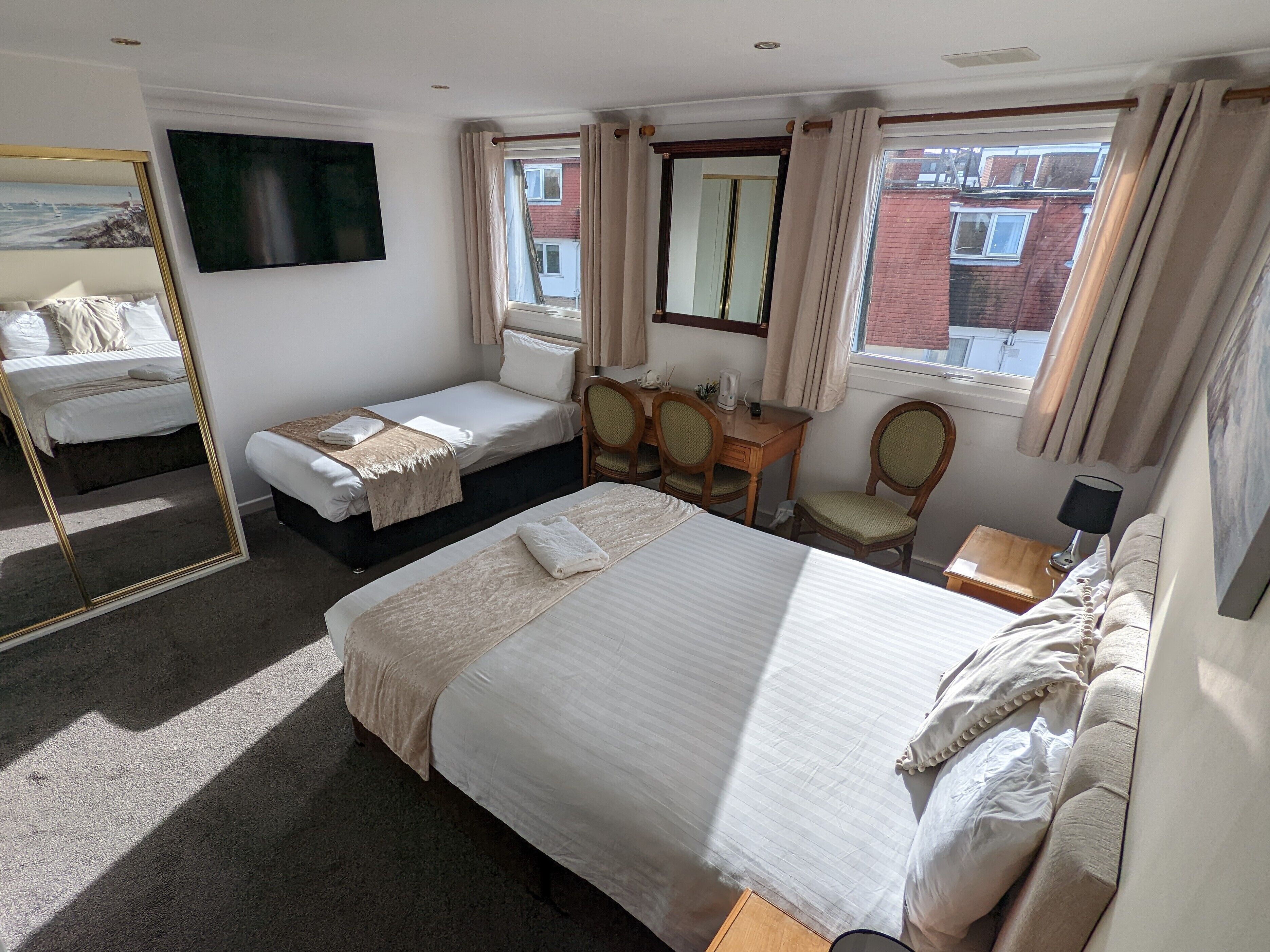 Een hotelkamer met een groot bed, een kleiner bed, een bureau met stoelen, een televisie en een raam met gordijnen.