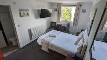 Una habitación de hotel con cama, escritorio, silla, televisor, ventana con cortinas y radiador.