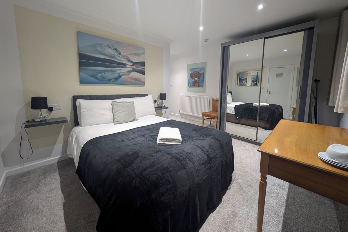 A hotel room with a bed, bedside table, lamp, artwork on the wall, and a sliding door.