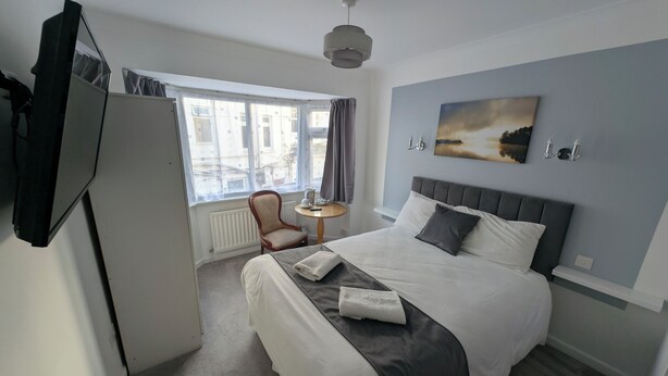 A hotel room with a bed, a chair, a small table, and a window with curtains. - Cecil Court Hotel (Bournemouth)