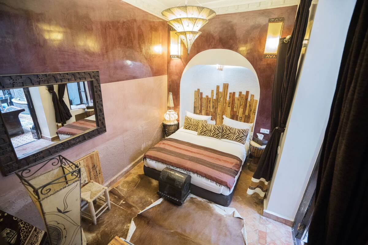 A bedroom with a large bed, a mirror, a bedside table, and a lamp.