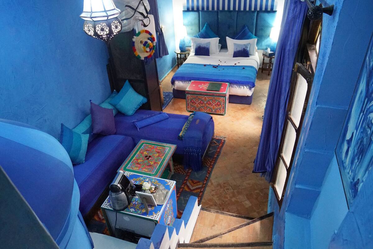 A room with a blue color scheme, featuring a sofa, a bed, and a small table with a decorative item.
