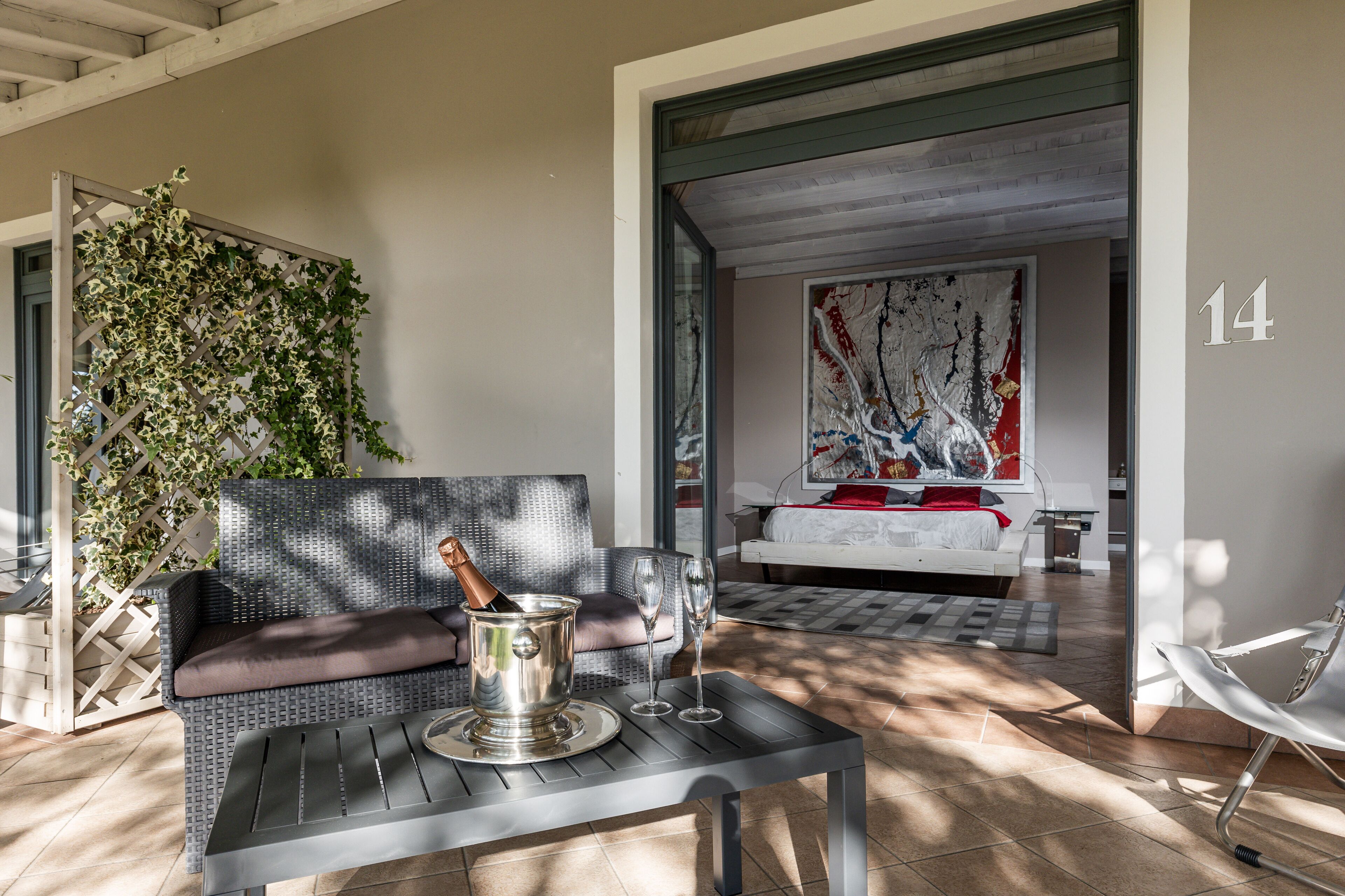 A modern room with a wicker sofa, a dining table with a champagne bucket, and a large abstract painting on the wall.