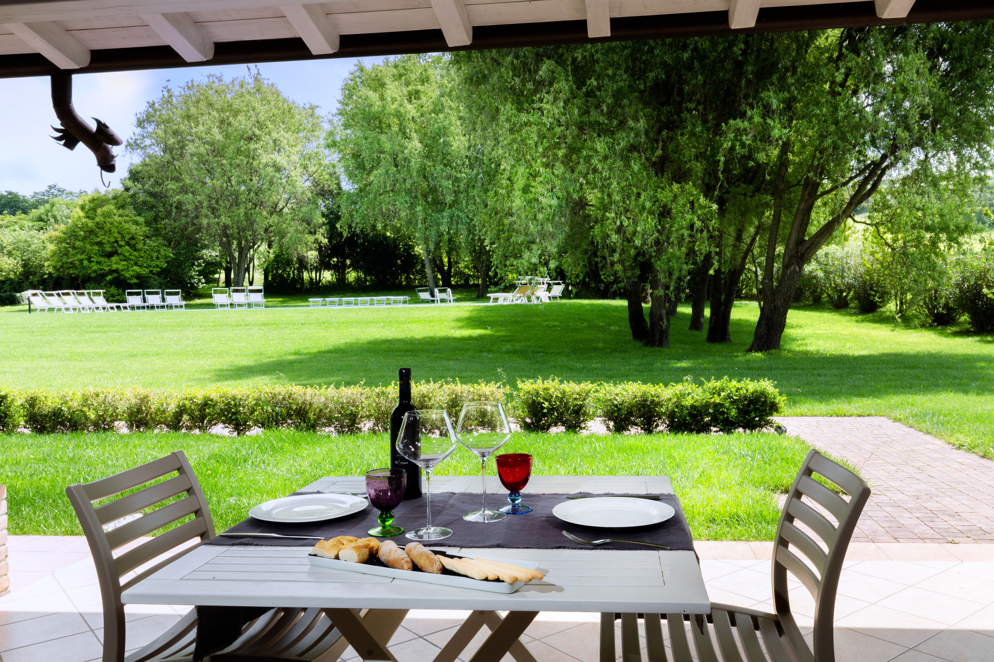 An outdoor dining area with a table set for two, a bottle of wine, and a basket of bread.