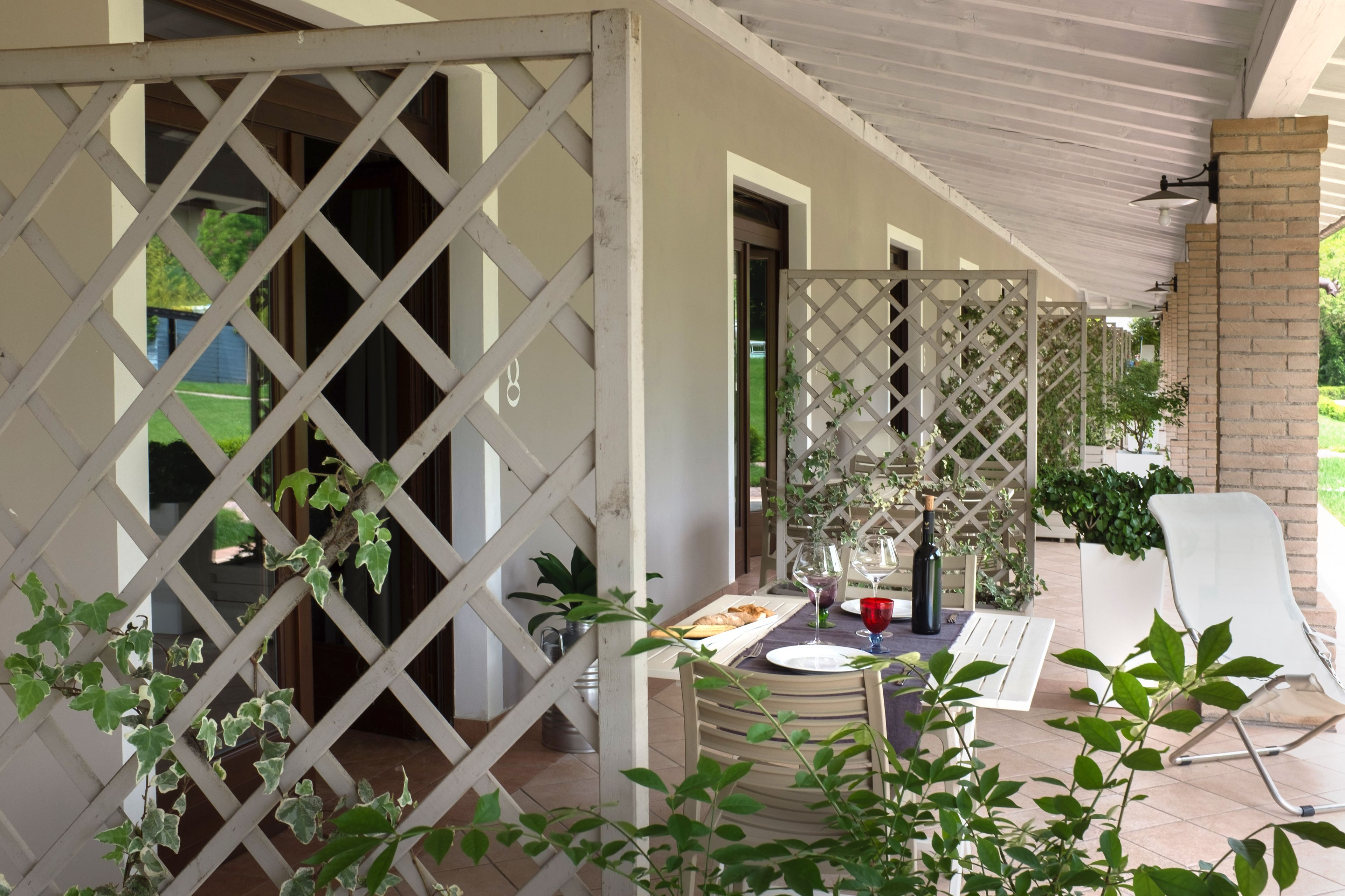 A covered outdoor dining area with a table set for two, a white chair, and a potted plant.