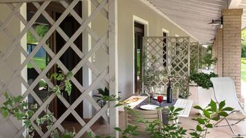 A covered outdoor dining area with a table set for two, a white chair, and a potted plant.