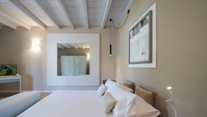 A bedroom with a large bed, a bedside table, a mirror, and a wall-mounted light.