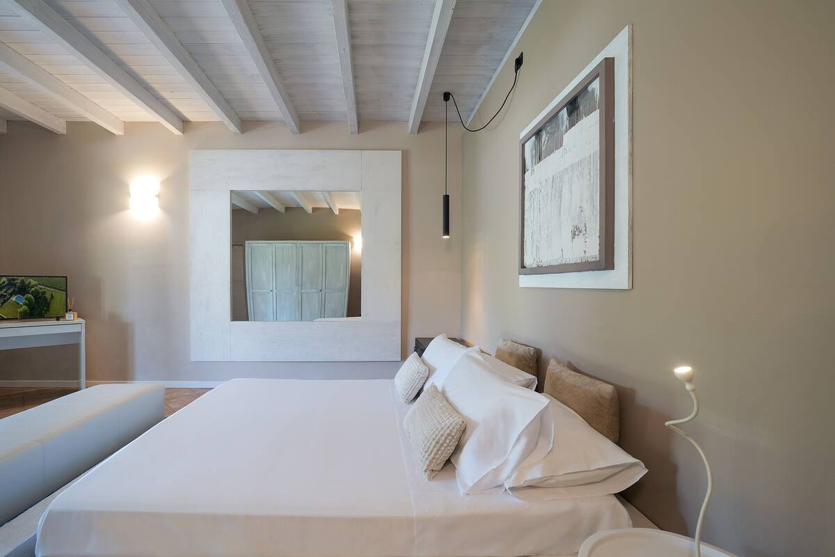 A bedroom with a large bed, a bedside table, a mirror, and a wall-mounted light.