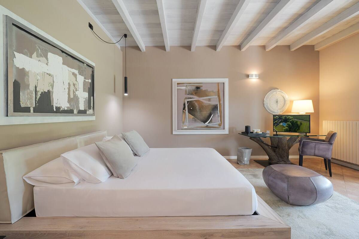 A bedroom with a large bed, a desk with a lamp, and a chair.