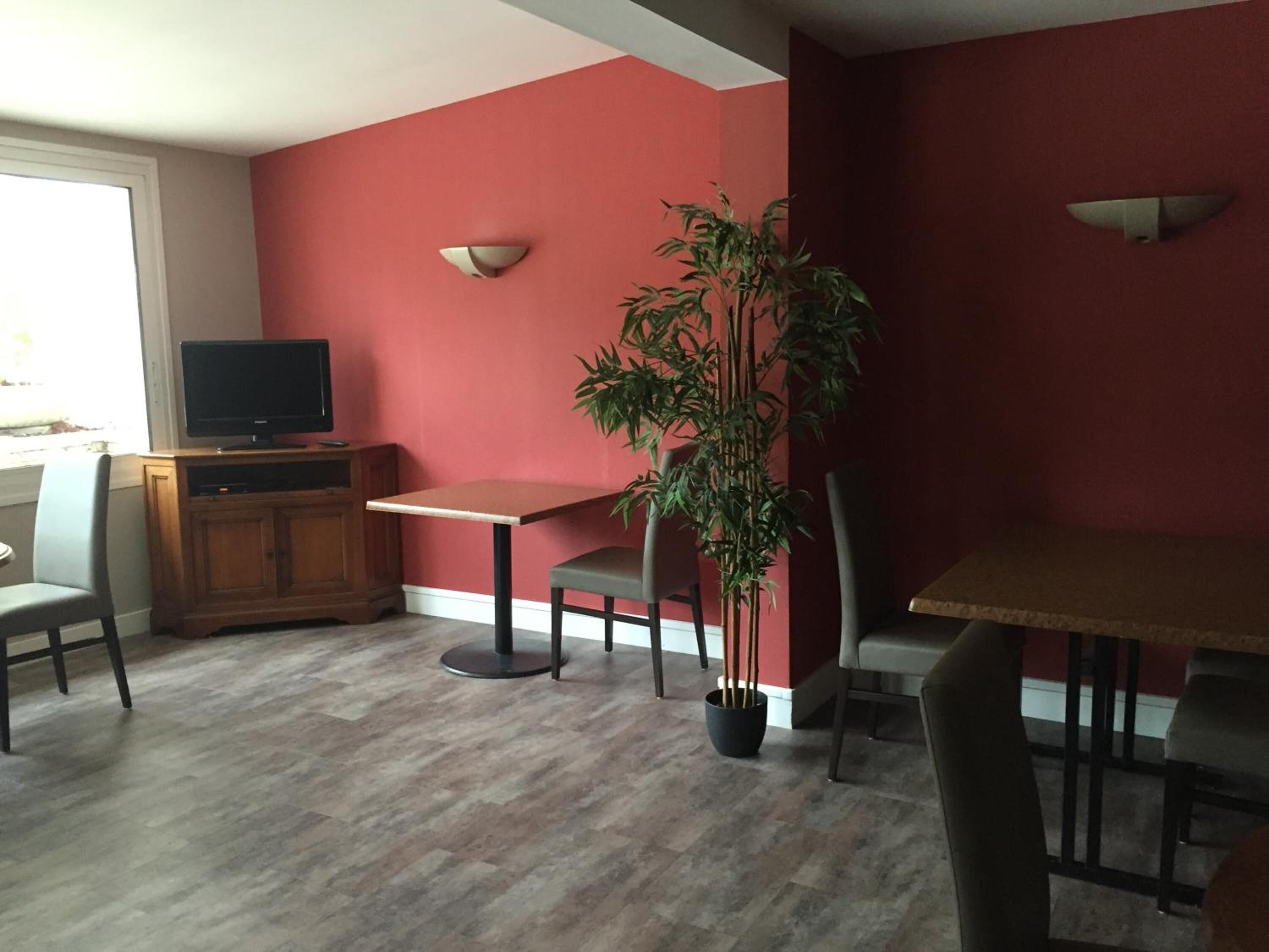 A dining area with a table and chairs, a television on a cabinet, and a potted plant.