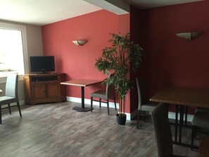Un comedor con una mesa y sillas, un televisor en un mueble y una planta en maceta.