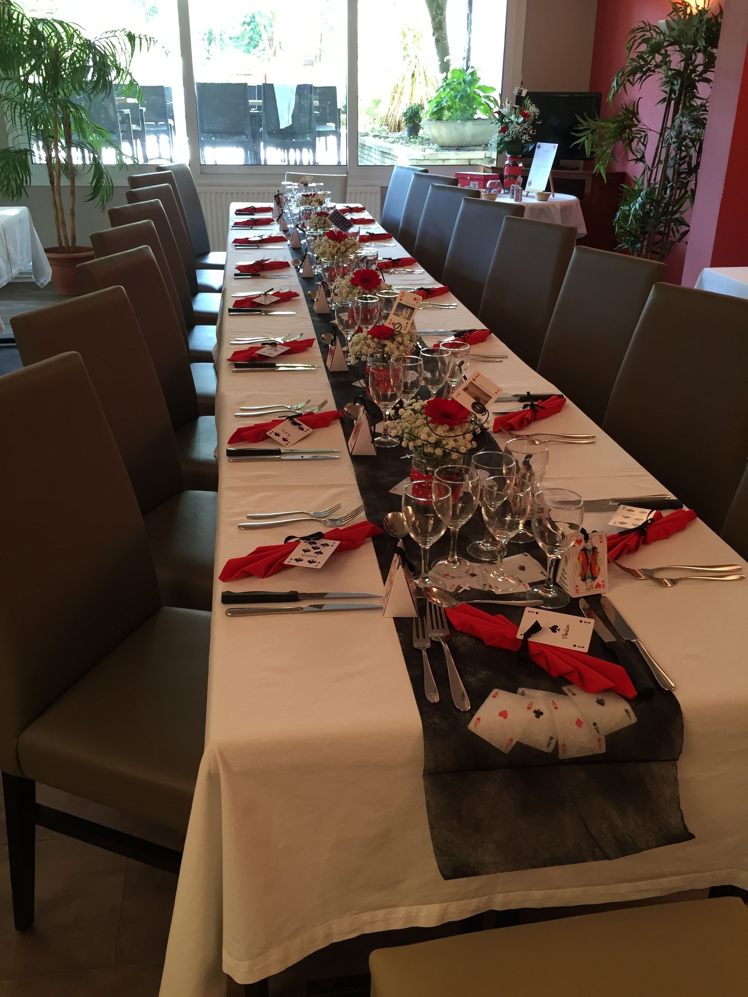A long dining table set with red napkins, silverware, and glassware, flanked by brown chairs.