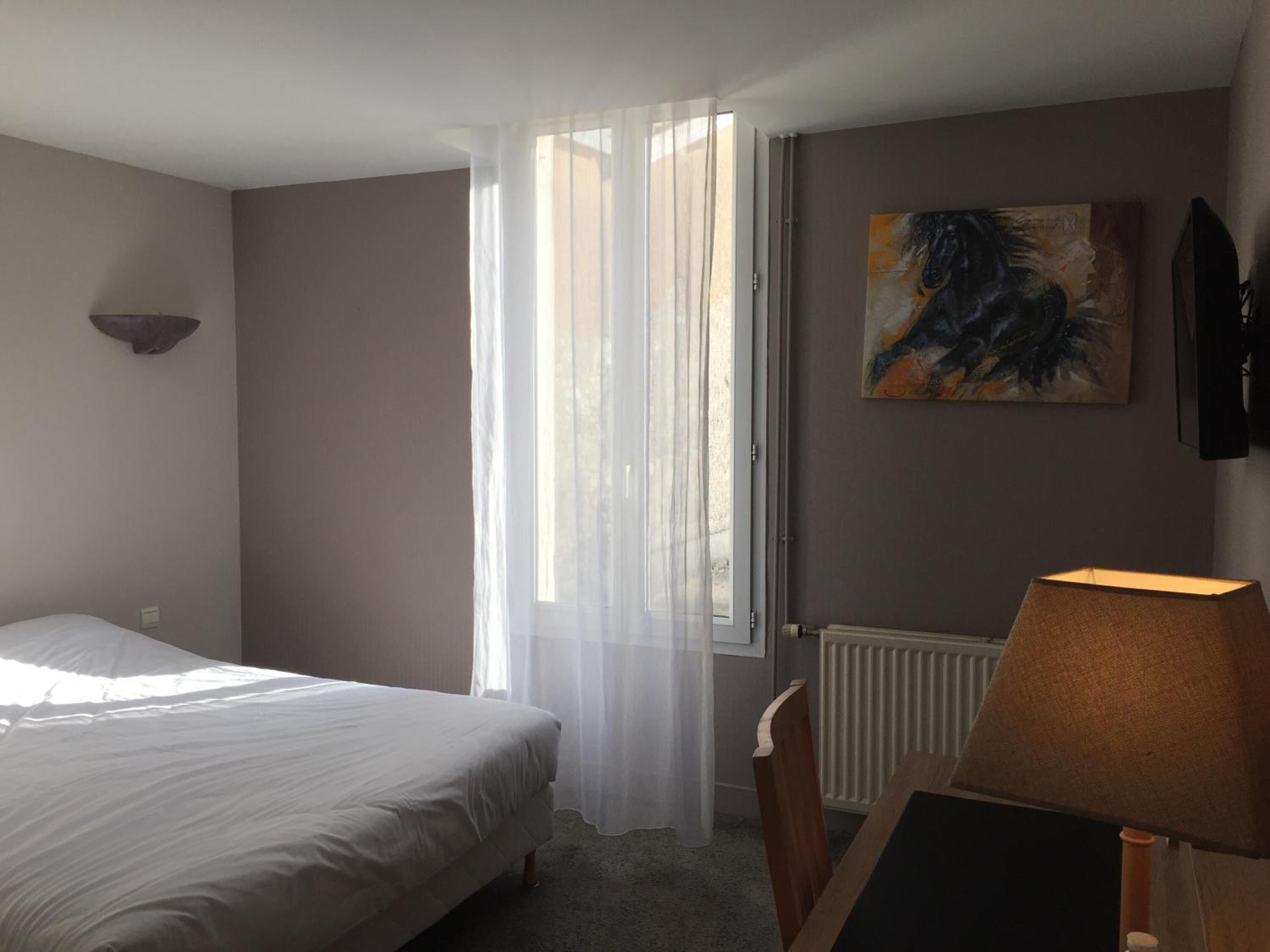 Et soveværelse med seng, et vindue med let gardin, en radiator, et maleri og en lampe.