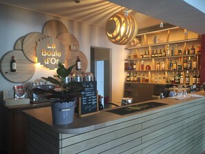Eine Bar mit einer Holztresen, Regalen voller Spirituosenflaschen, einer Kreidetafel mit der Speisekarte und einer Pendelleuchte.