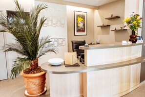 A reception desk with a palm plant, a framed poster, and a vase with flowers. - Auberge Bienvenue (Doué-en-Anjou)