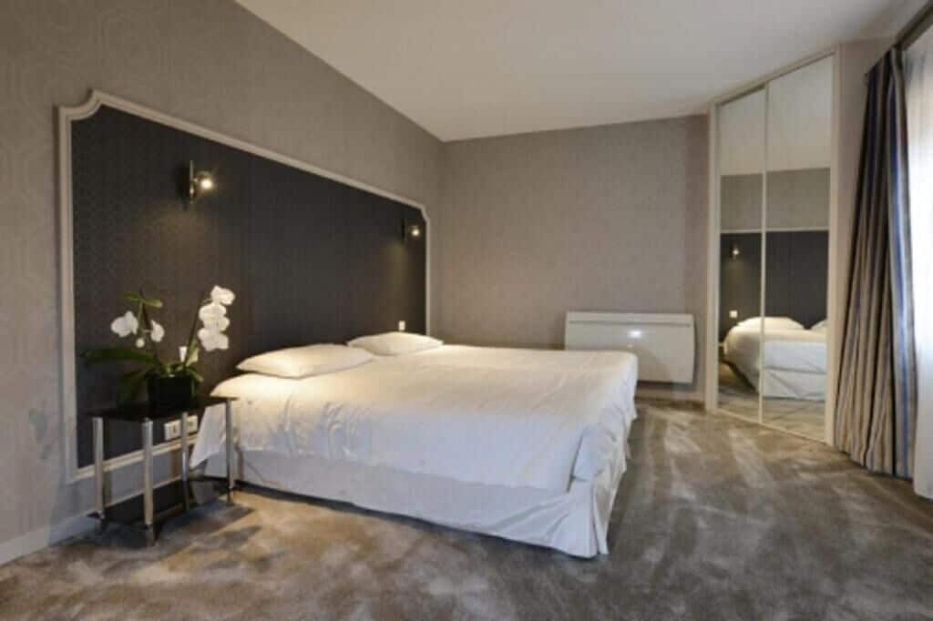 A modern hotel room with a large bed, a bedside table, a mirror, and a potted plant.