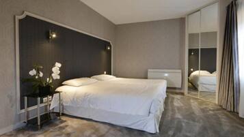 A modern hotel room with a large bed, a bedside table, a mirror, and a potted plant.