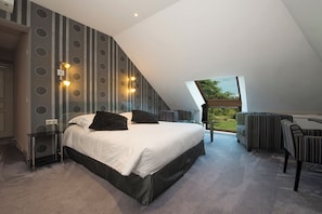 A bedroom with a large bed, a seating area with striped sofas, and a view through a skylight. - Auberge Bienvenue (Doué-en-Anjou)